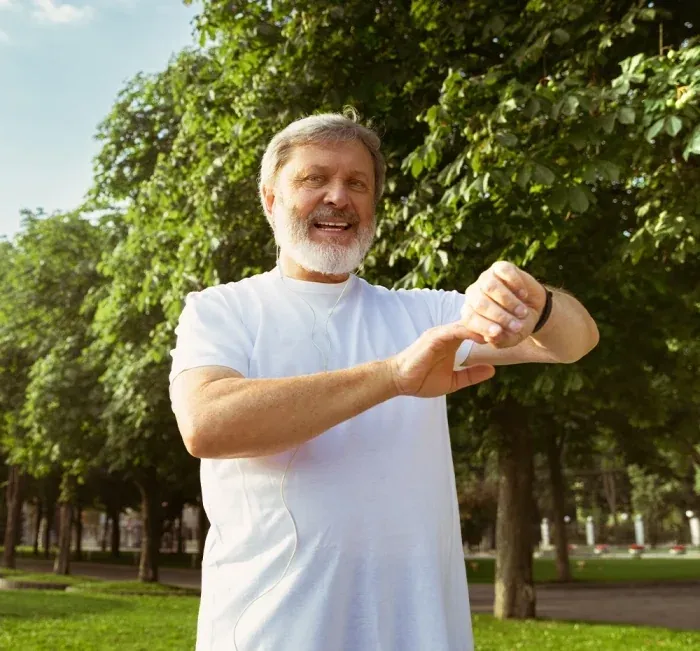 An older man in a park stretching his arms over his head on a sunny day